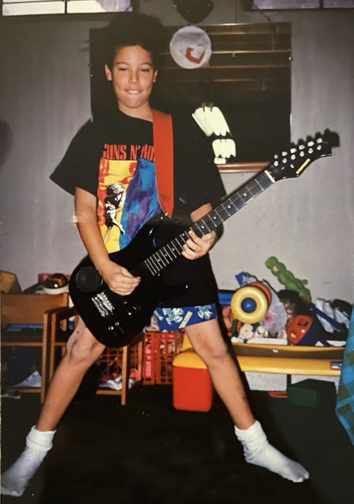 Childhood photo of Double Down Mac playing his first electric guitar at home.