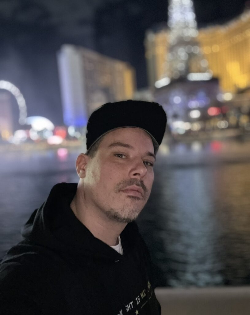 Double Down Mac standing in front of the Bellagio Fountains and Paris Las Vegas at night.