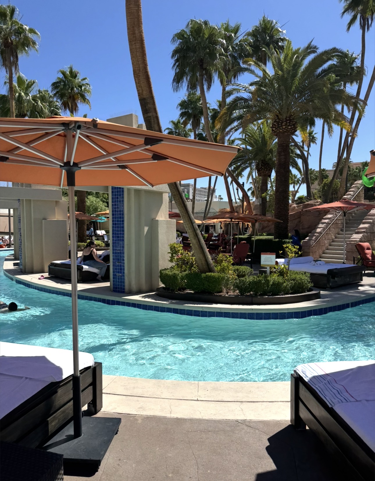 MGM Grand Las Vegas lazy river surrounded by palm trees, orange umbrellas, and poolside lounge chairs.