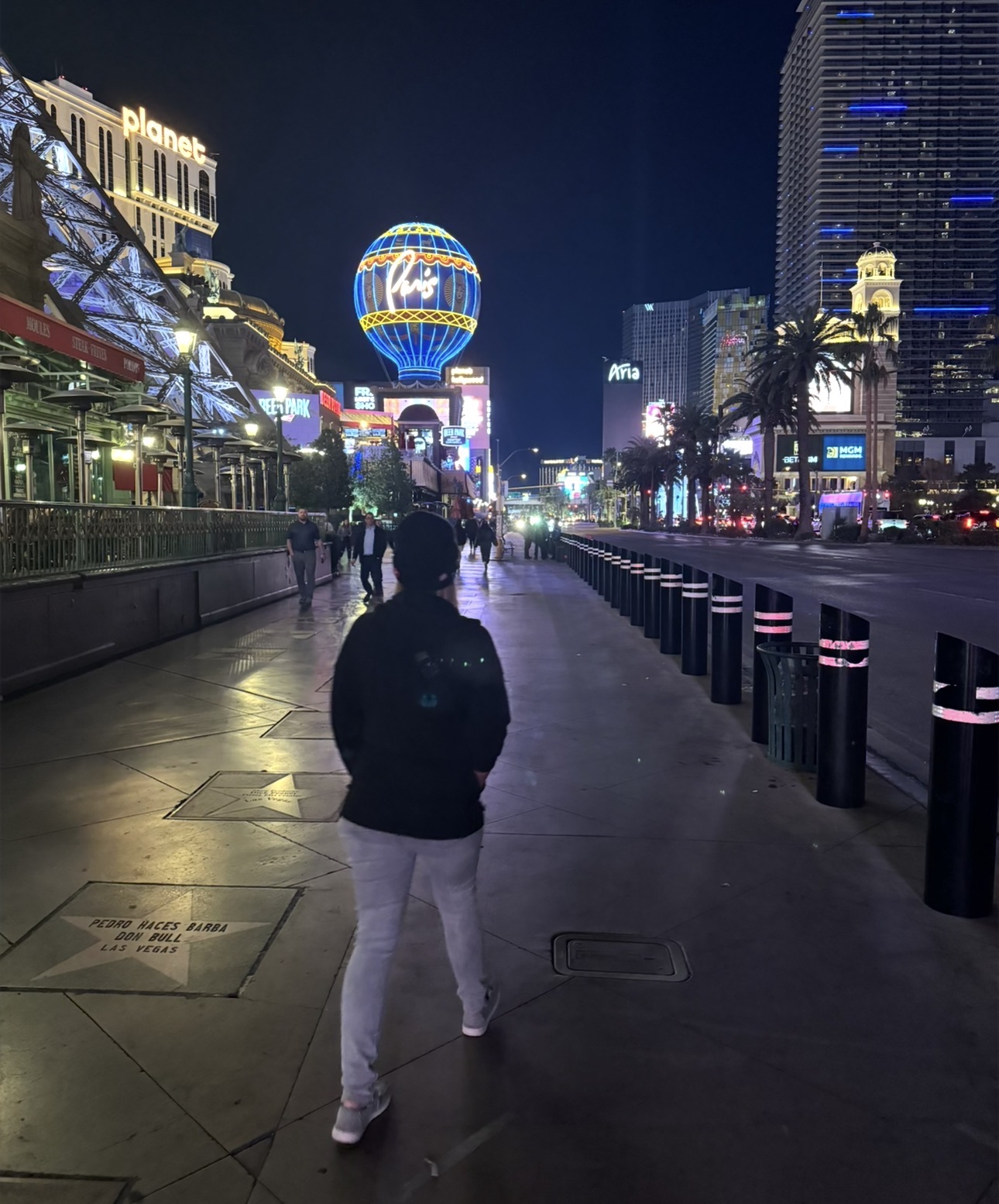 Walking along the Las Vegas Strip at night toward the illuminated Paris Las Vegas balloon.